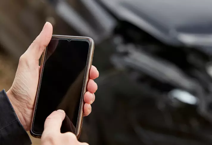 Hånd som berører en mobil-skjerm foran en bil